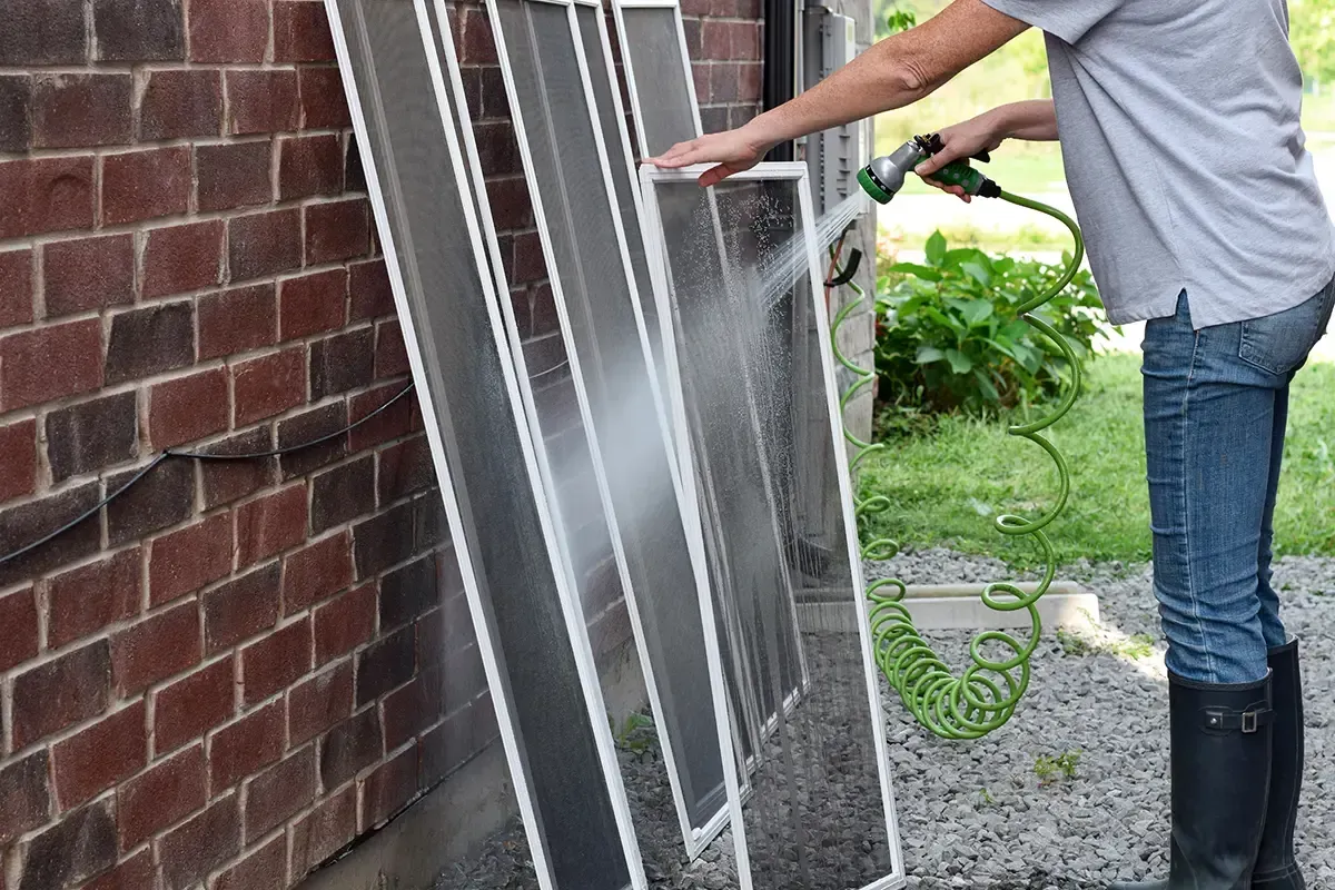 Person power-washing a metal gate beside a brick wall and garden path