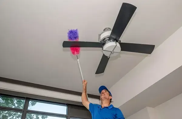 Person dusting a ceiling fan with a red and purple duster in a room