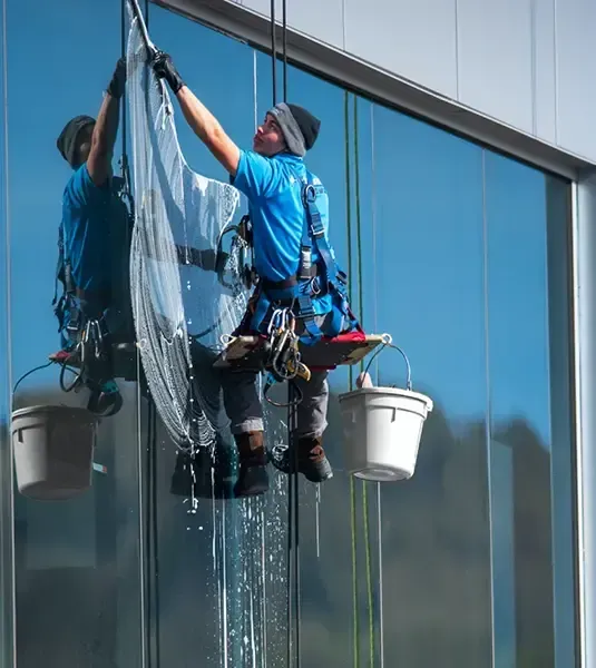 Window washer suspended from cables cleaning a tall building's glass facade.