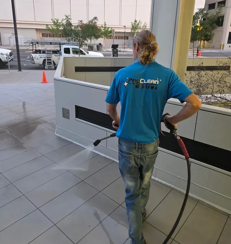 Person pressure washing a stone patio beside a modern house