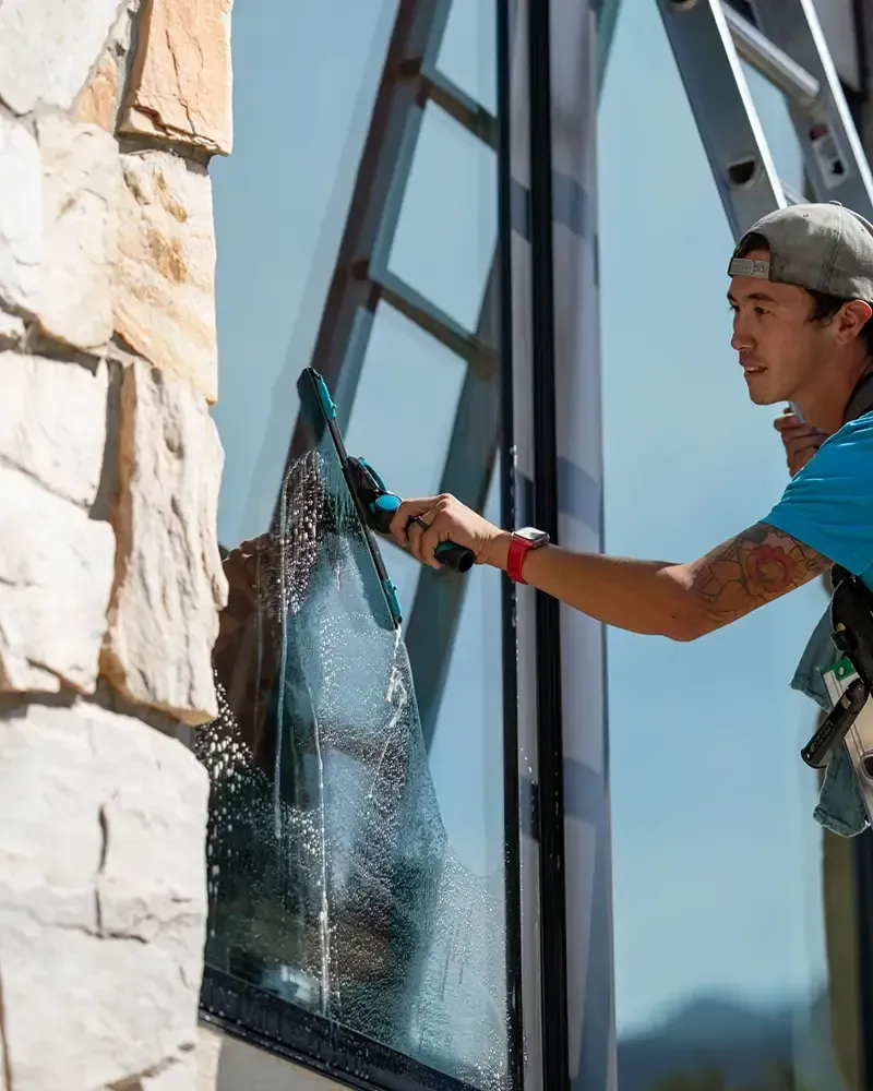 Two window washers on a curved building, suspended by ropes, cleaning glass.