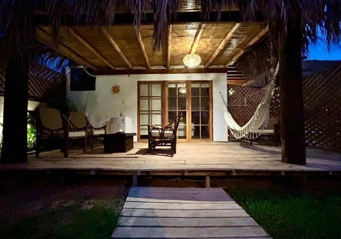 Terraza de madera con techo de paja, sillas y hamaca. Puertas que dan al interior.