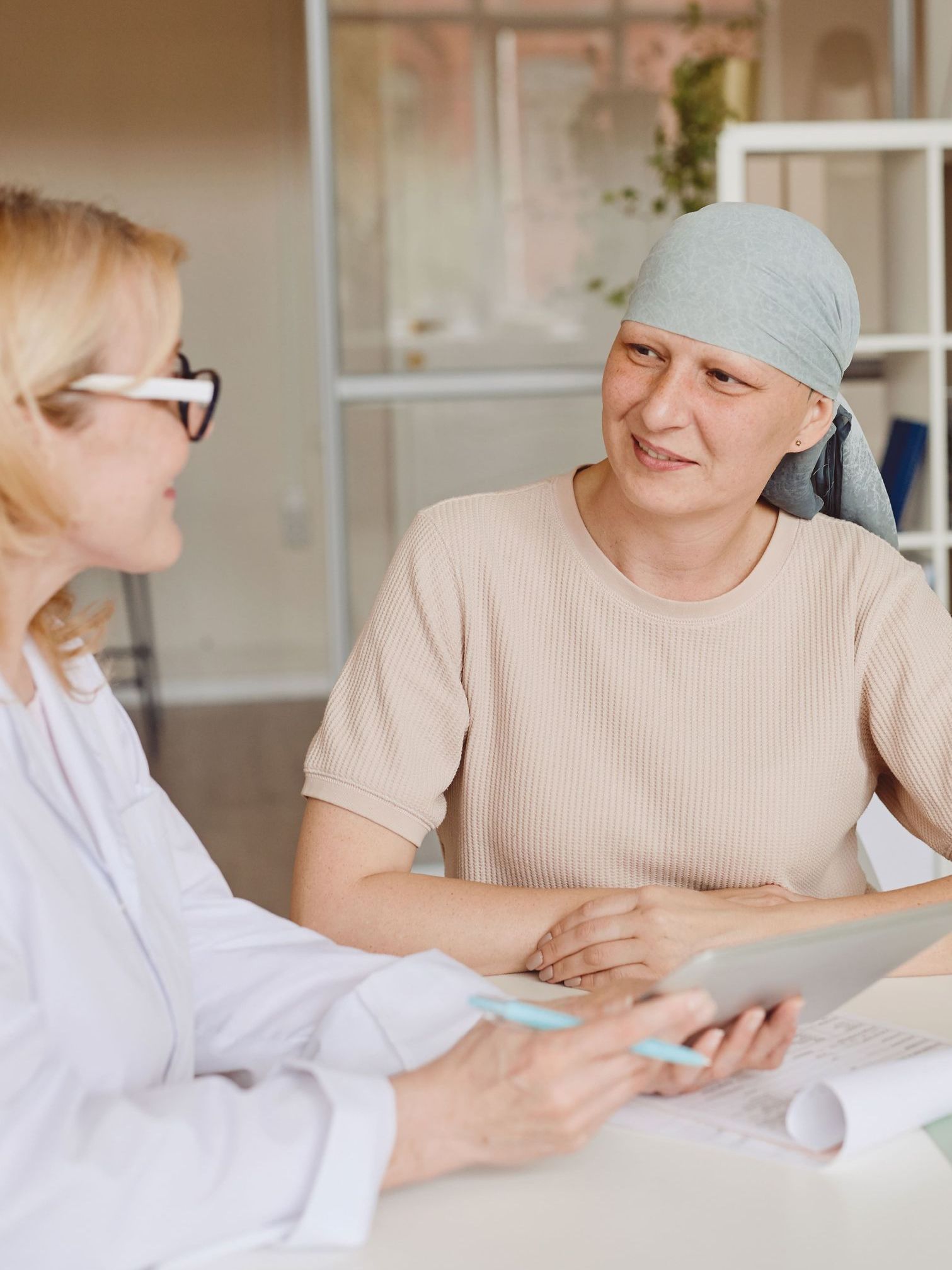 A woman with cancer is sitting at a table talking to a doctor.