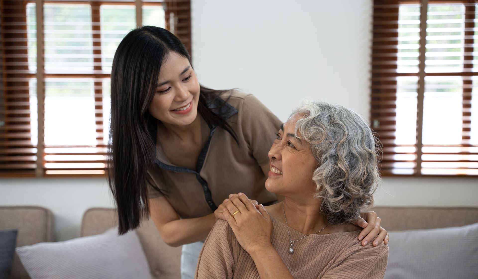 A young woman is standing next to an older woman on a couch.