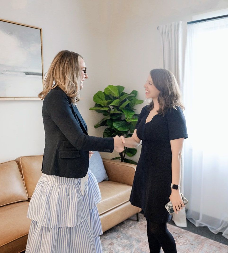 Two women shaking hands in a living room with a couch