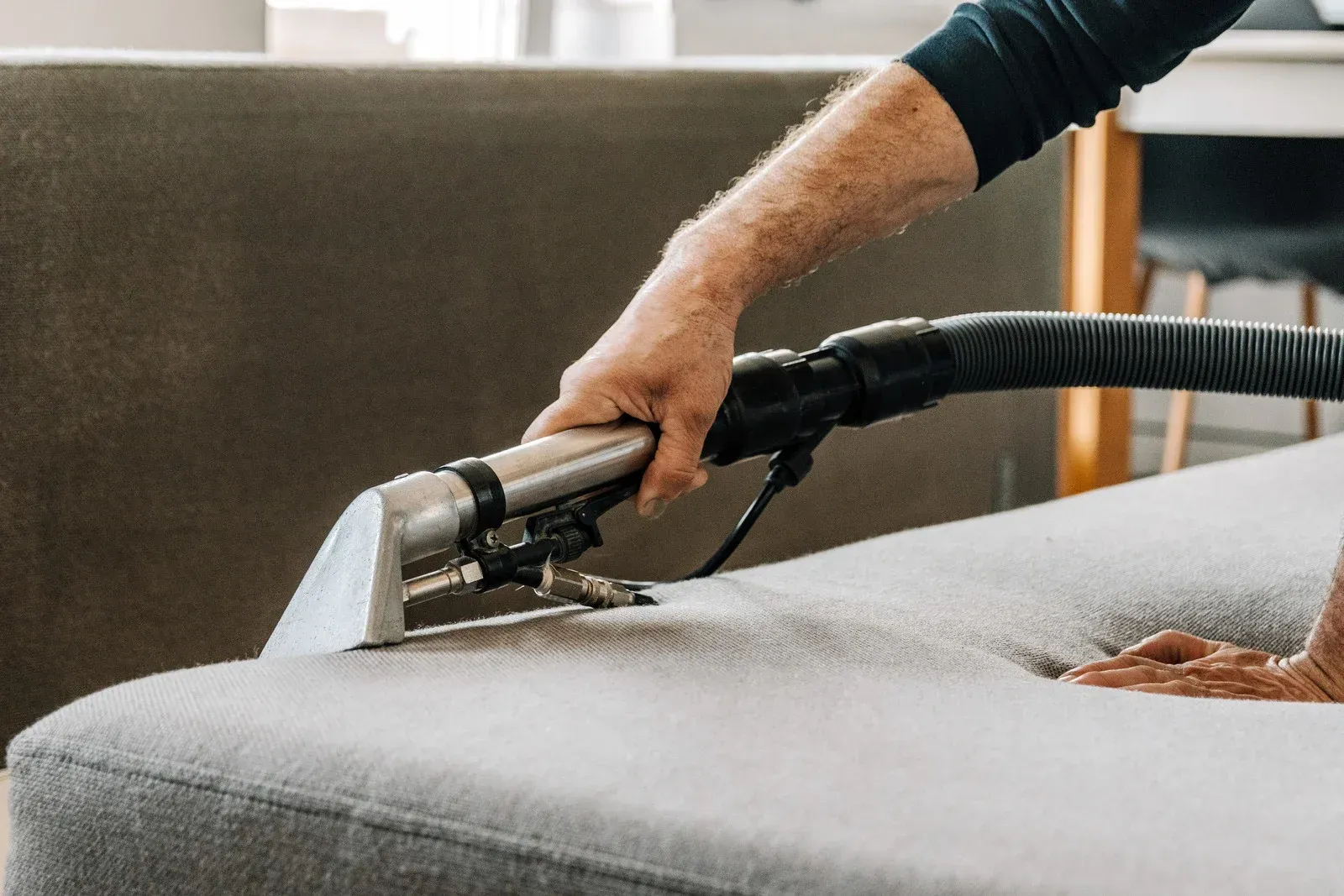 Person cleaning a light gray couch with a steam cleaner.