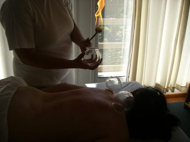 Two people in a dim room, one receiving a massage near a sunlit window.