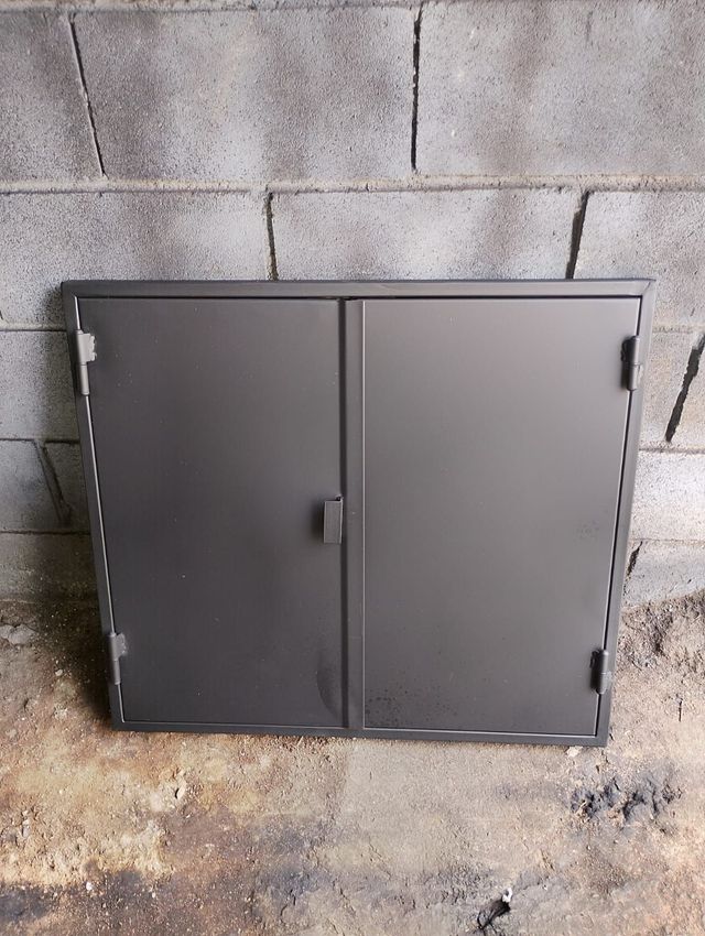 Armario de almacenamiento de metal gris contra una pared de bloques de hormigón sobre un suelo de hormigón.
