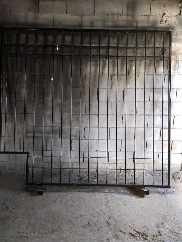 Una gran puerta metálica negra apoyada contra una pared de hormigón en una habitación industrial austera.