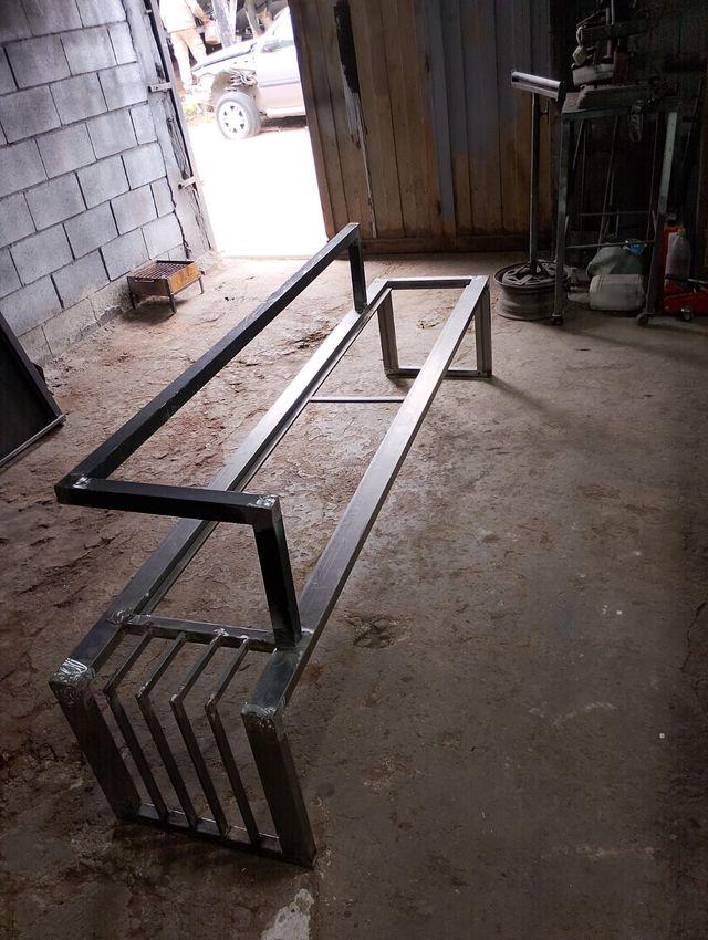 Banco de metal con asiento de listones, colocado sobre un suelo de hormigón en la entrada de un garaje.