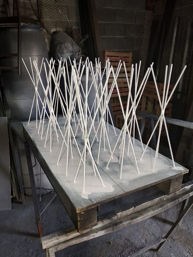 Estructuras triangulares de alambre blanco dispuestas sobre una mesa de metal en un taller industrial.
