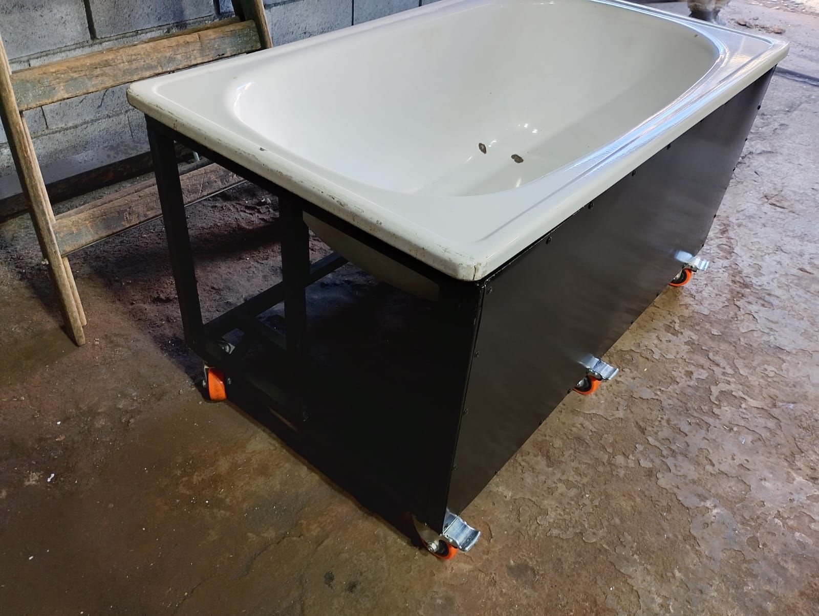 Bañera blanca sobre un soporte negro en un taller o garaje.