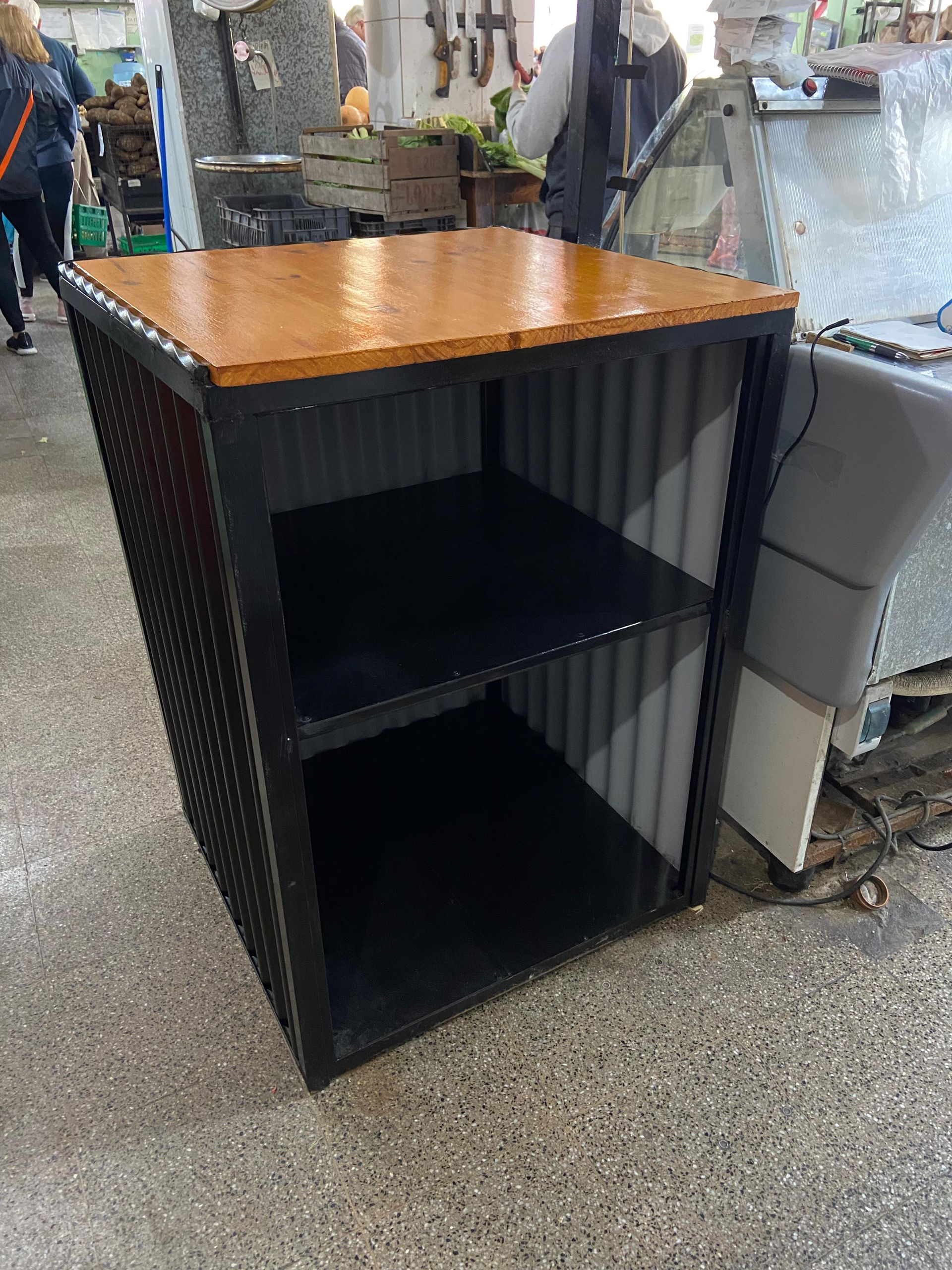 Vitrina negra con tapa de madera y dos estantes en un taller o pasillo de tienda.