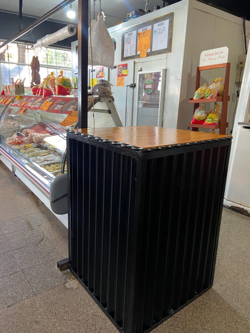 Mostrador negro acanalado en una charcutería o mercado, con vitrinas y estantes para la carne al fondo.
