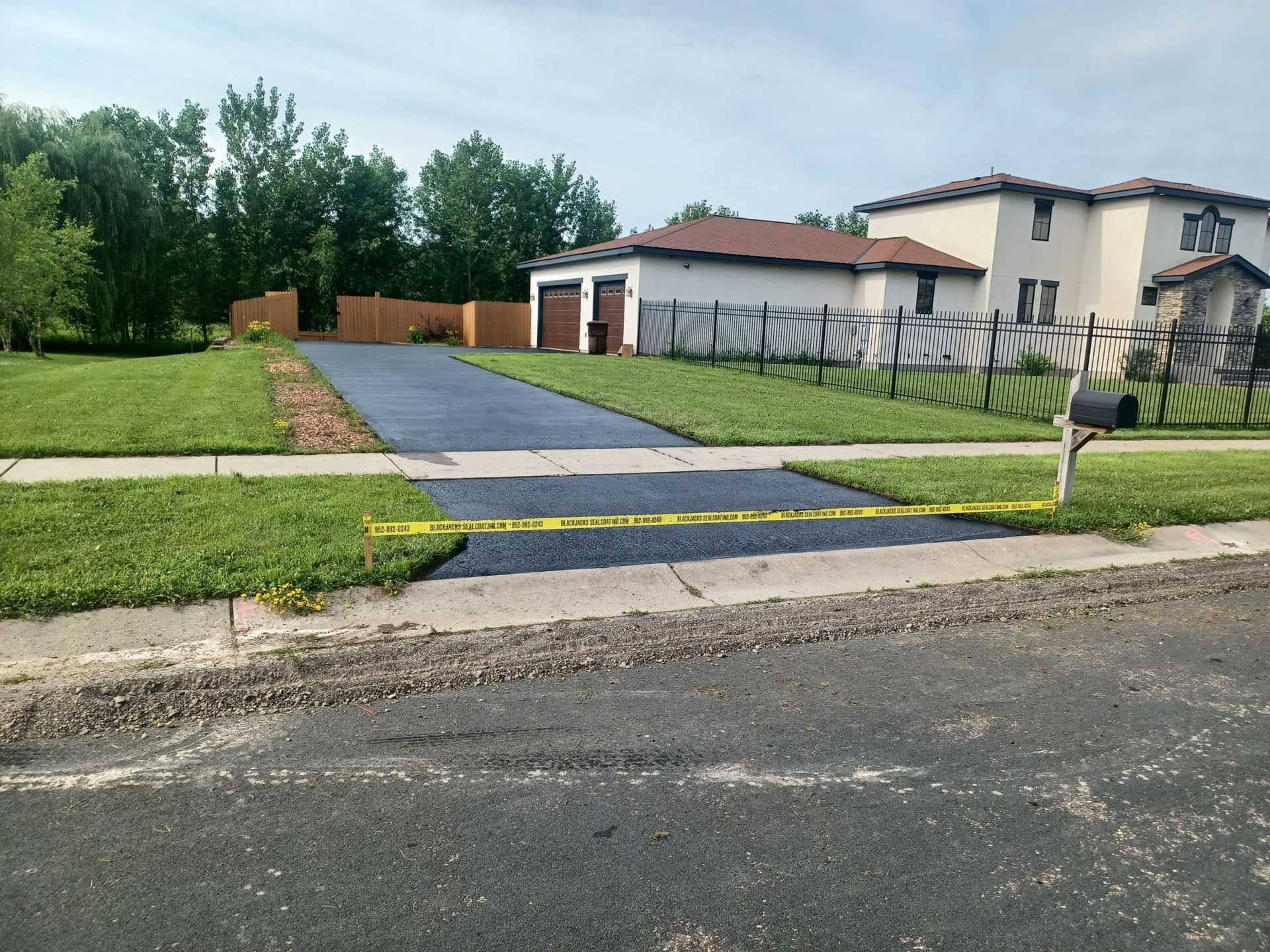 Residential driveway with yellow caution tape blocking a sidewalk crossing, beside a house and lawn