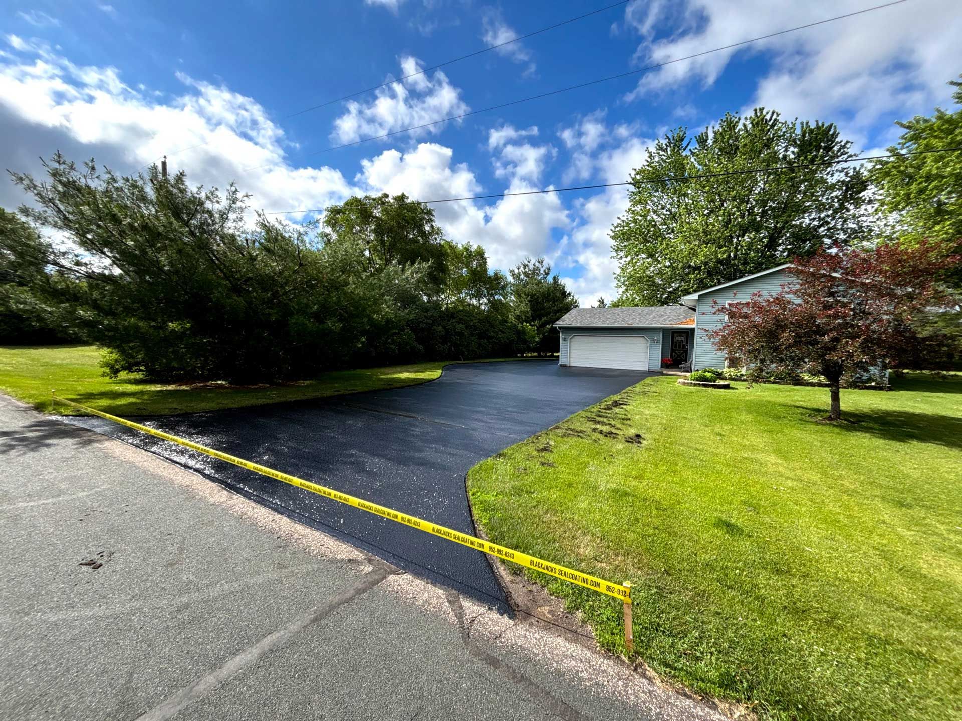 Residential driveway leading to a white garage, bordered by green lawn and trees under a blue sky