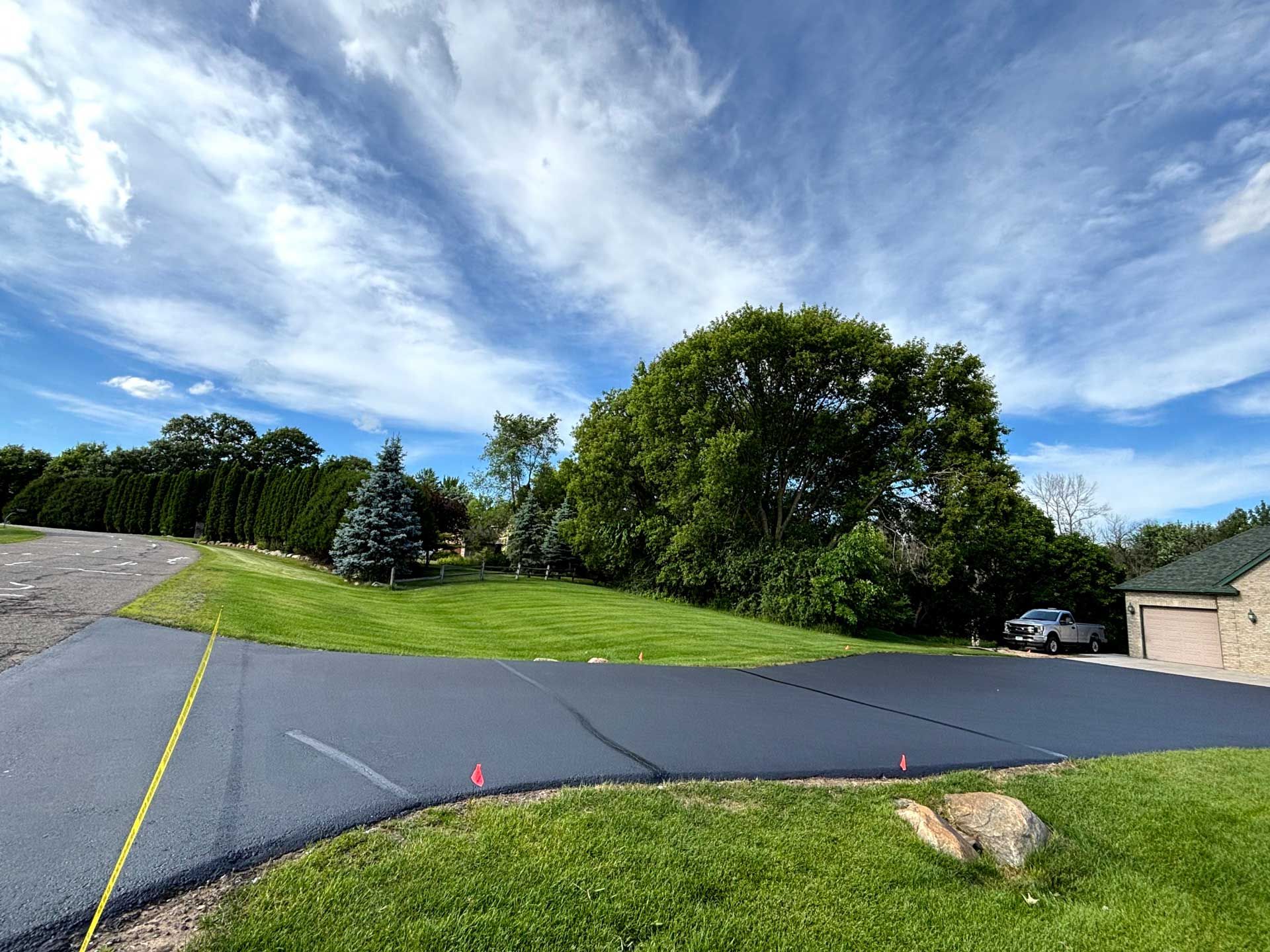 Driveway beside green lawn and trees under a bright, cloudy sky