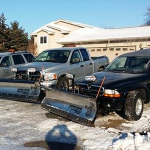 Three snow plows are parked in front of a house.