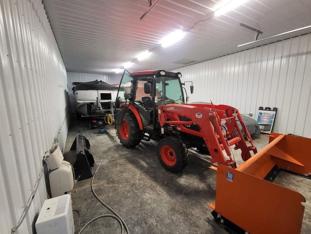 Red tractor with front loader inside a white storage container, with an orange attachment in the foreground.