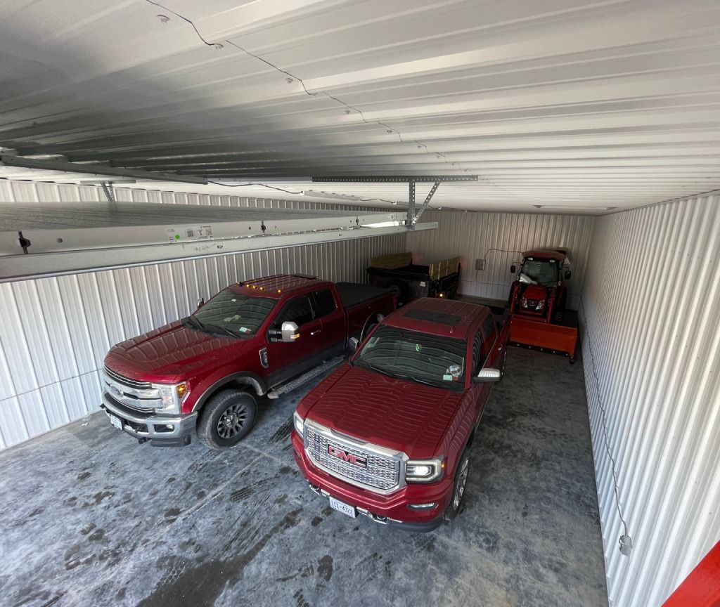 Three red pickup trucks parked inside a corrugated metal shipping container.
