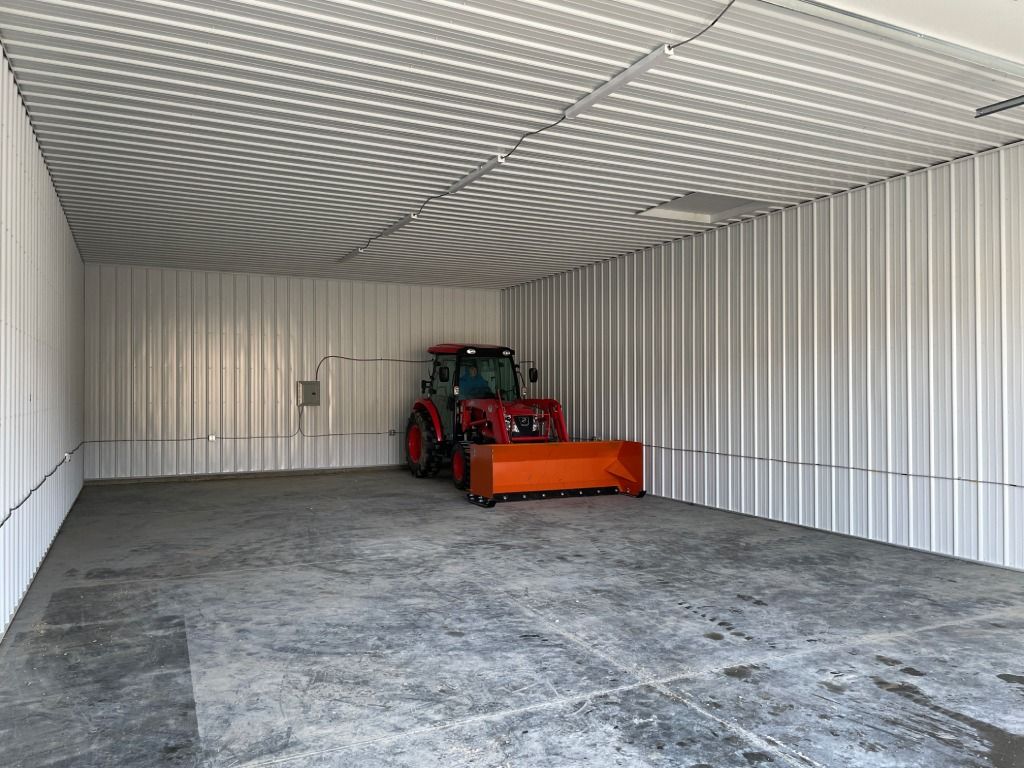 Red tractor with orange attachment in an empty metal storage container