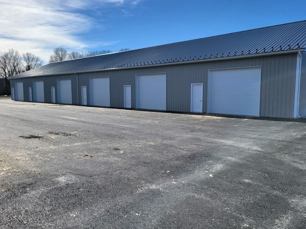 Row of gray storage unit doors on a metal building beside an empty paved lot under a blue sky