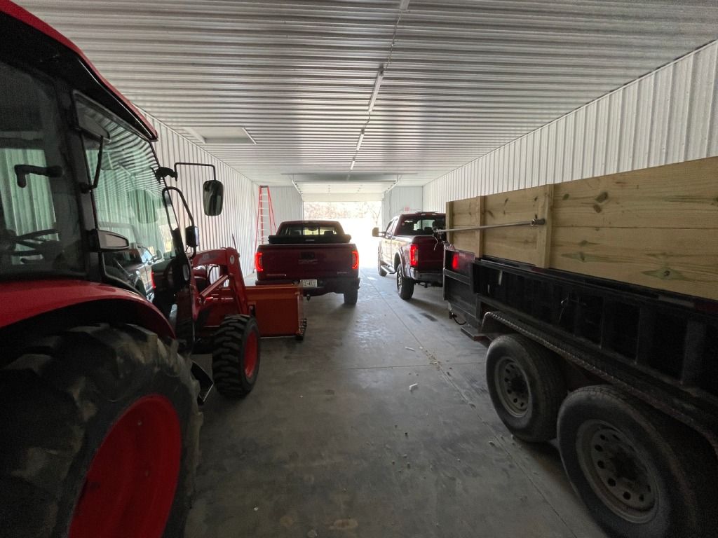 Tractors and trailers parked inside a barn-like garage with a concrete floor and corrugated metal walls