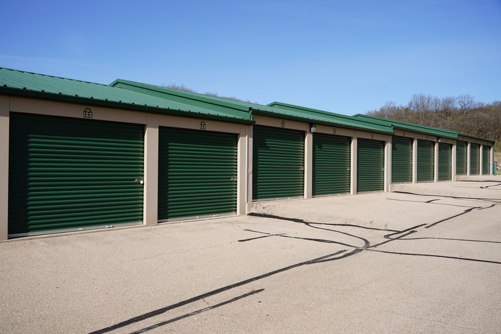 Row of green storage unit doors along a paved lot under a clear sky