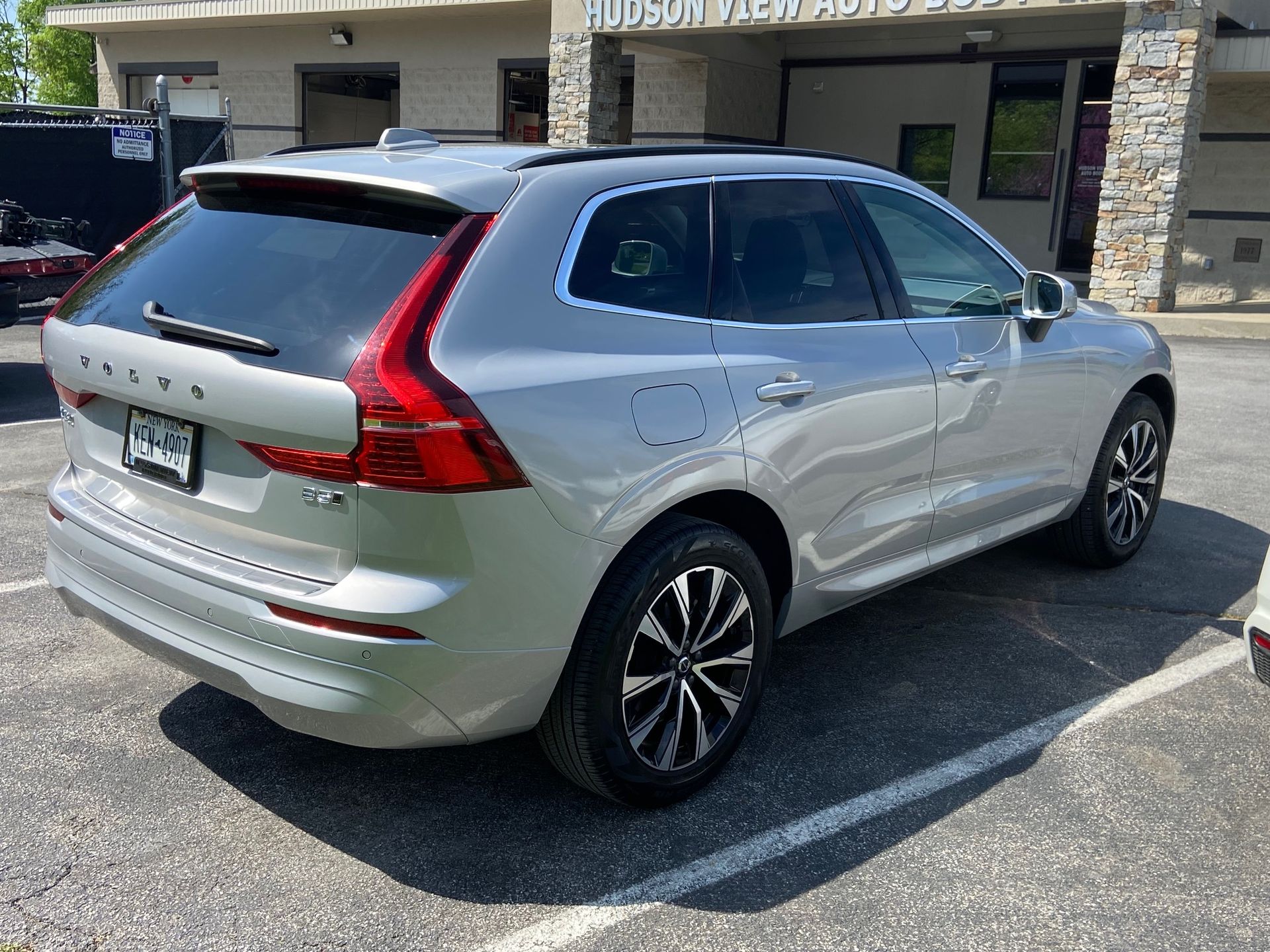A silver Volvo XC60 SUV parked in a paved lot in front of a stone and tan building.