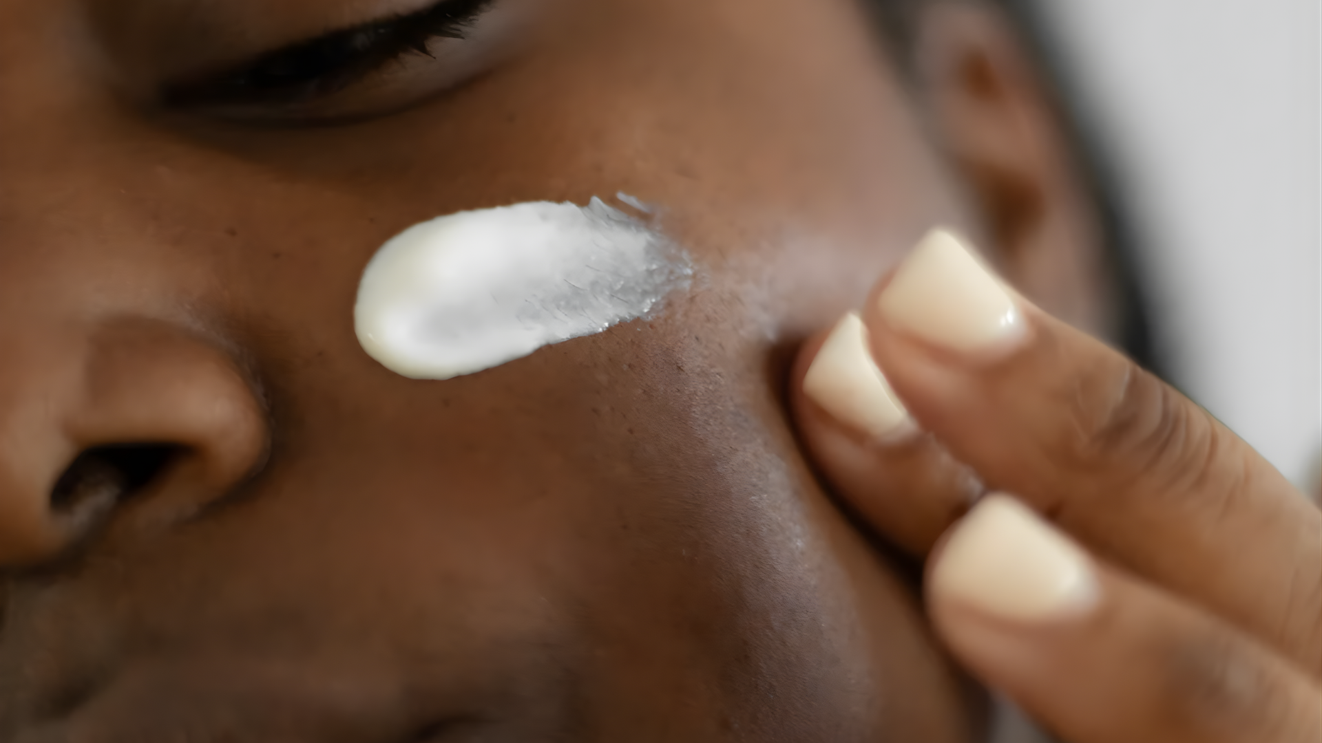 Person applying white cream to cheek with fingers
