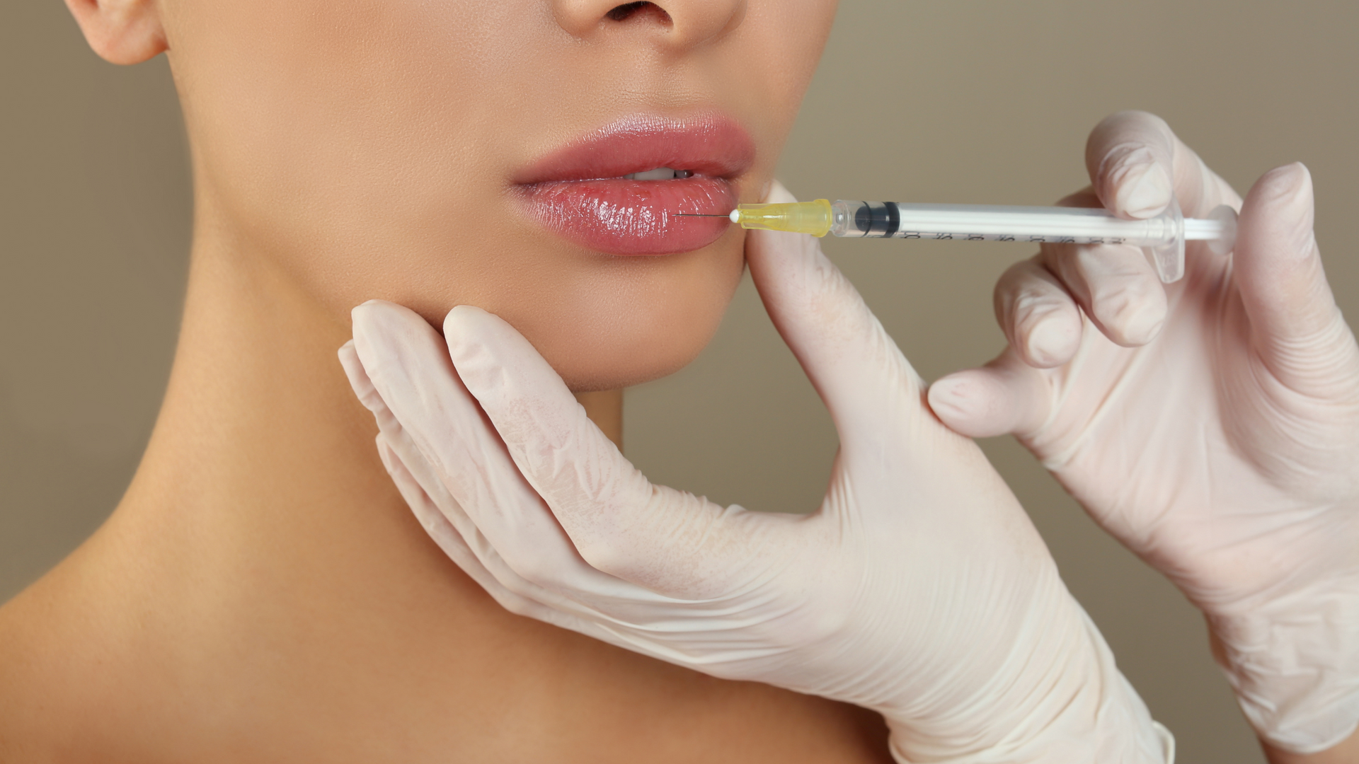 Person receiving lip filler injection. Hands wearing gloves inject lips with syringe.