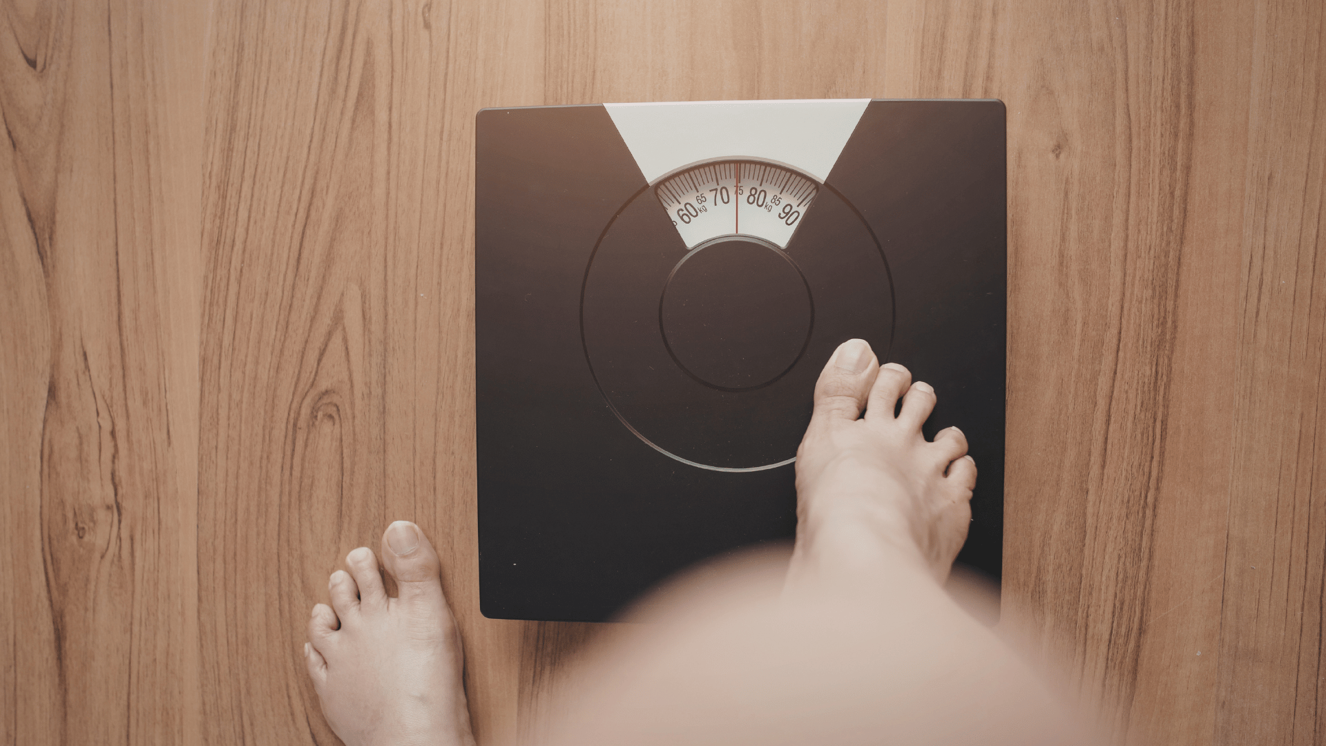 Feet standing on a black bathroom scale on a wooden floor, with the dial visible.