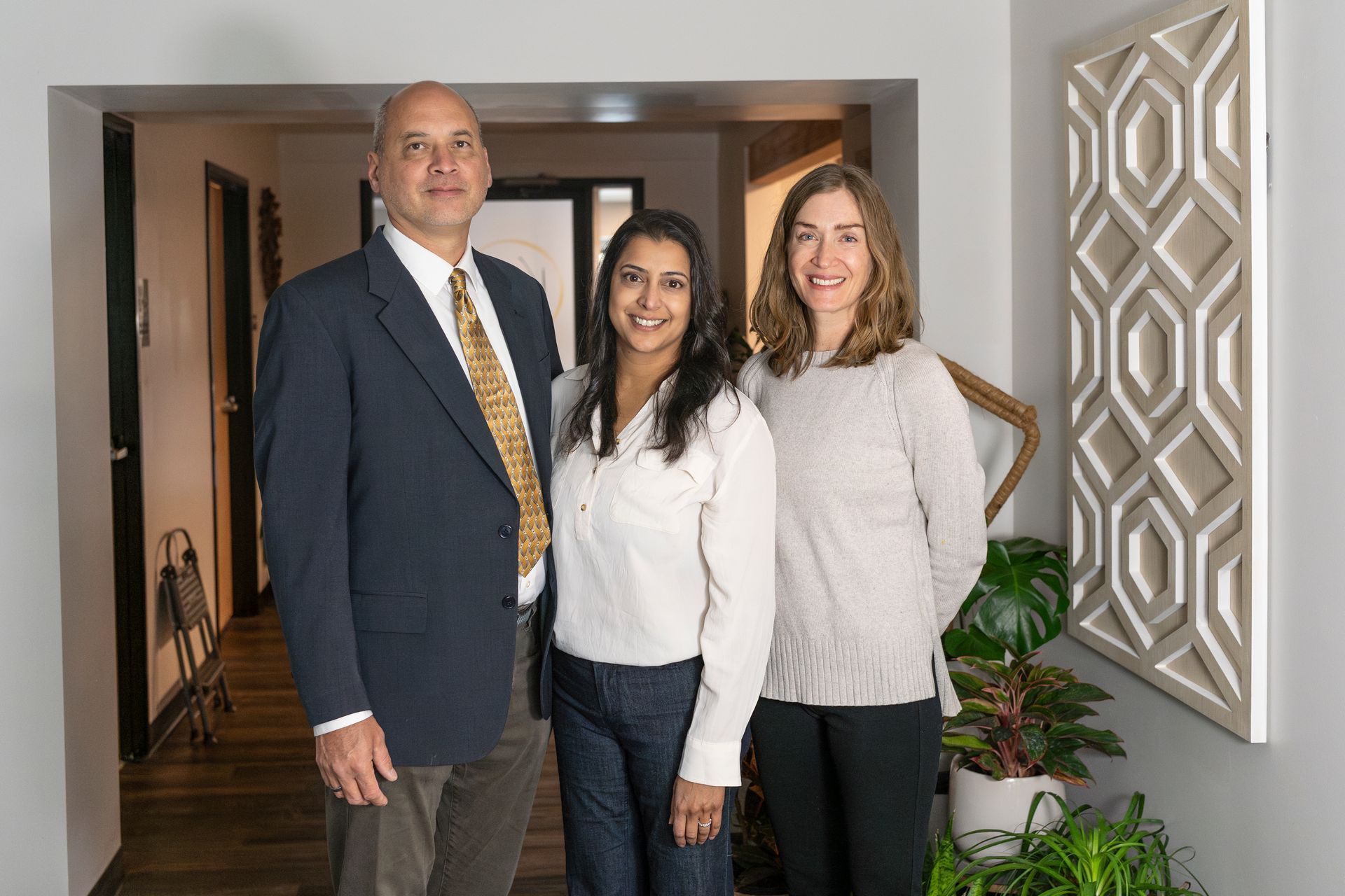 Three people standing together in a hallway, smiling at the camera.