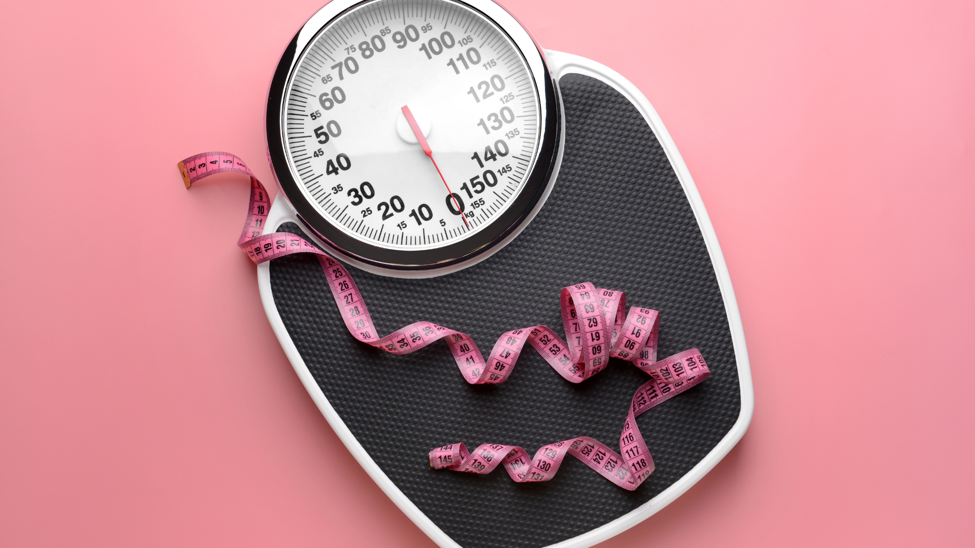 Tape measure and coiled pink measuring tape on a black textured surface with a pink background