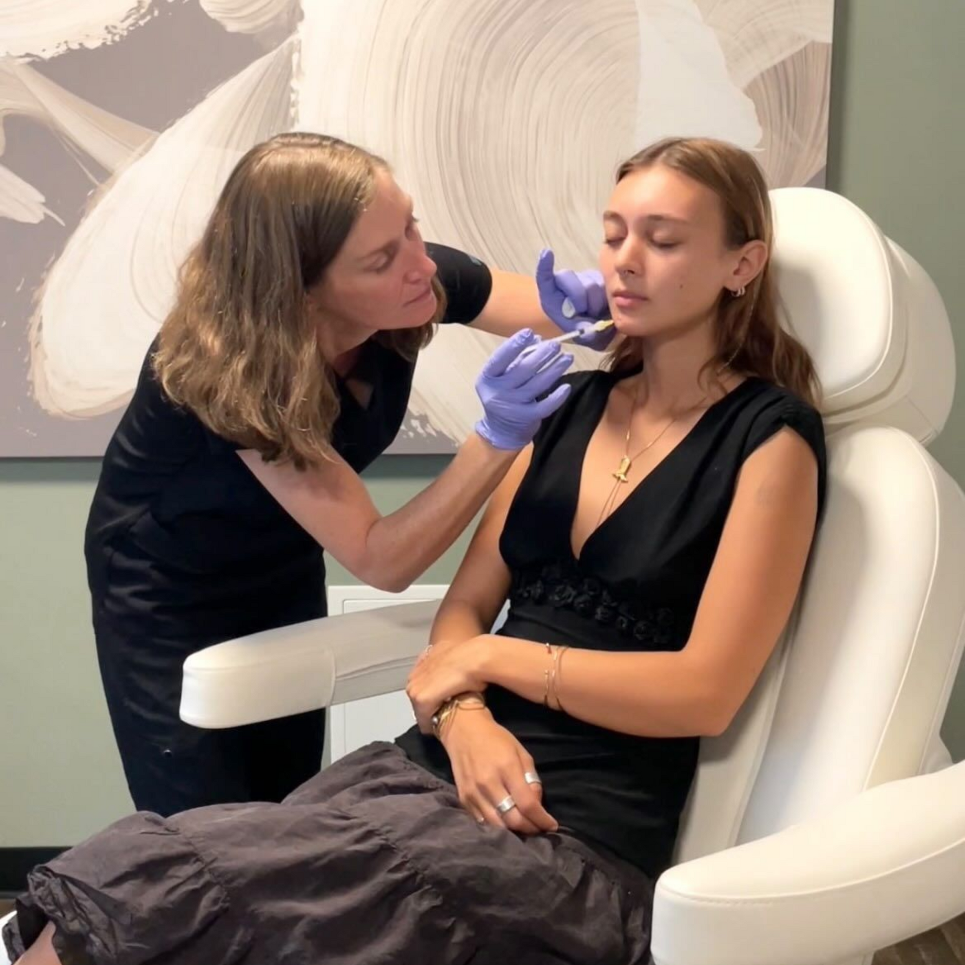 A clinician applies a treatment to a seated patient’s cheek in a bright clinic chair.