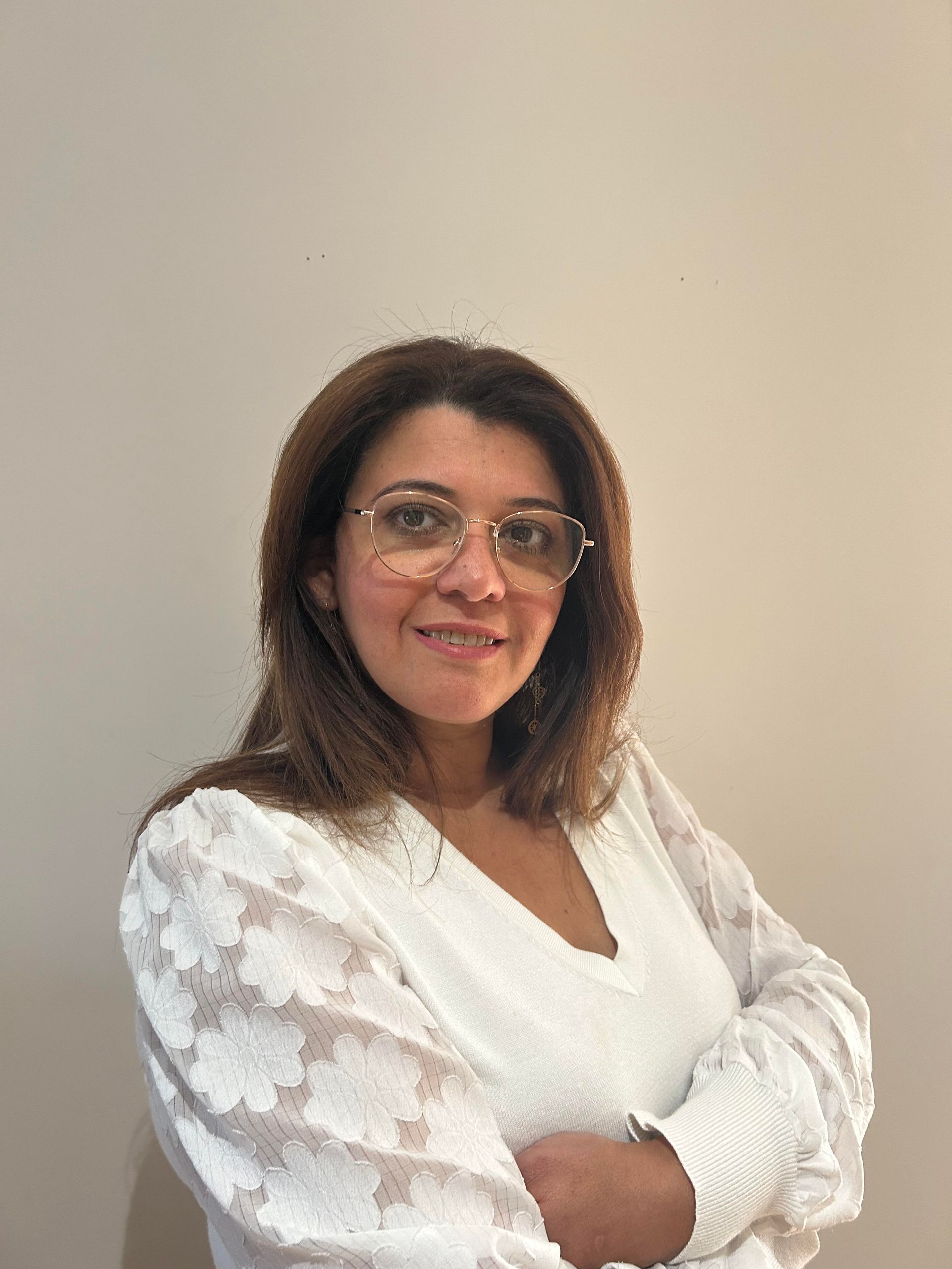 Woman wearing glasses and a white blouse, smiling with arms crossed.