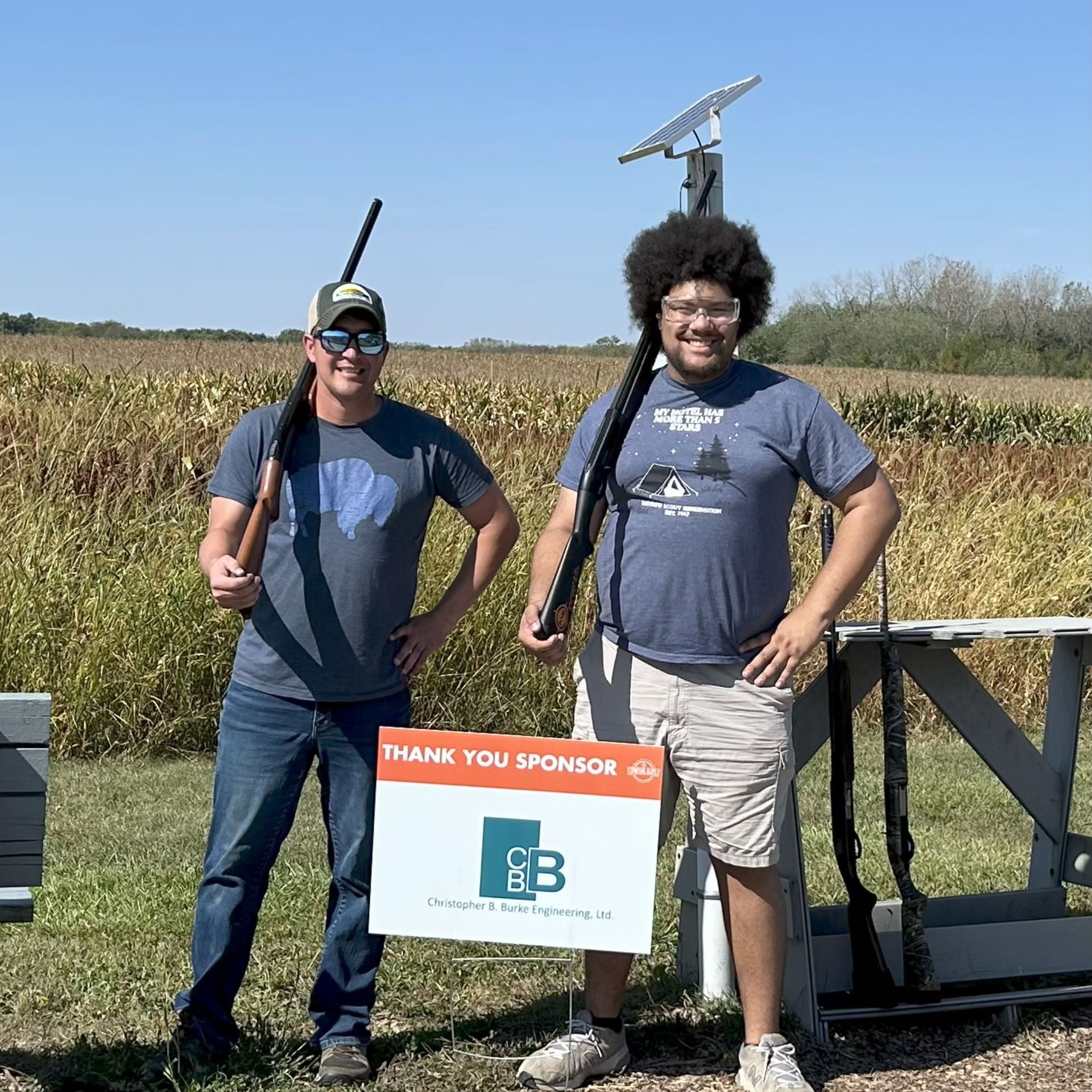 People shooting shotguns at a range; some wearing safety gear, standing on a grassy field.