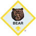 Bear rank patch, showing a brown bear head on a light blue diamond, surrounded by a yellow border.