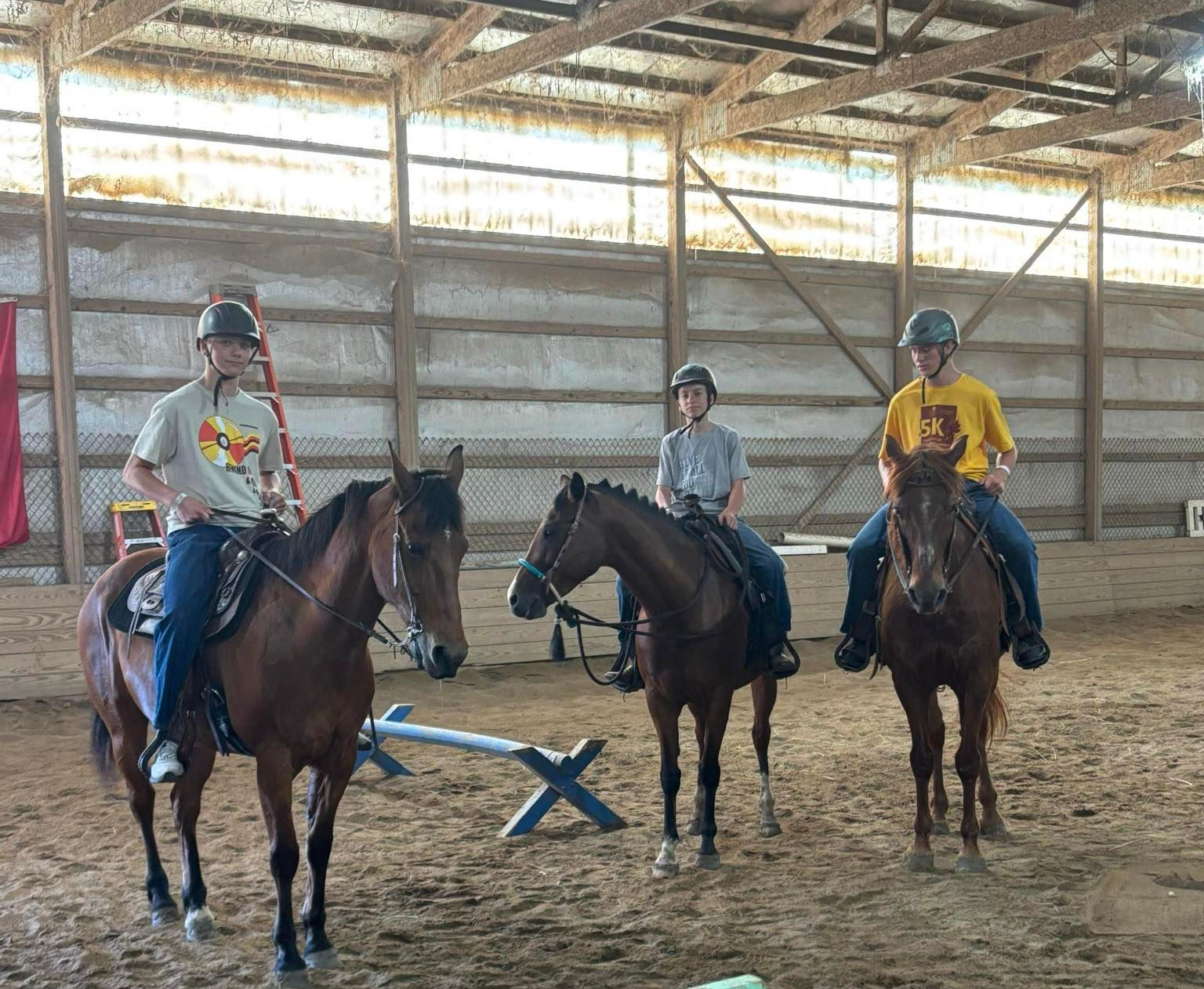 Three riders on horseback in an indoor riding arena. They are wearing helmets and are looking at the camera.
