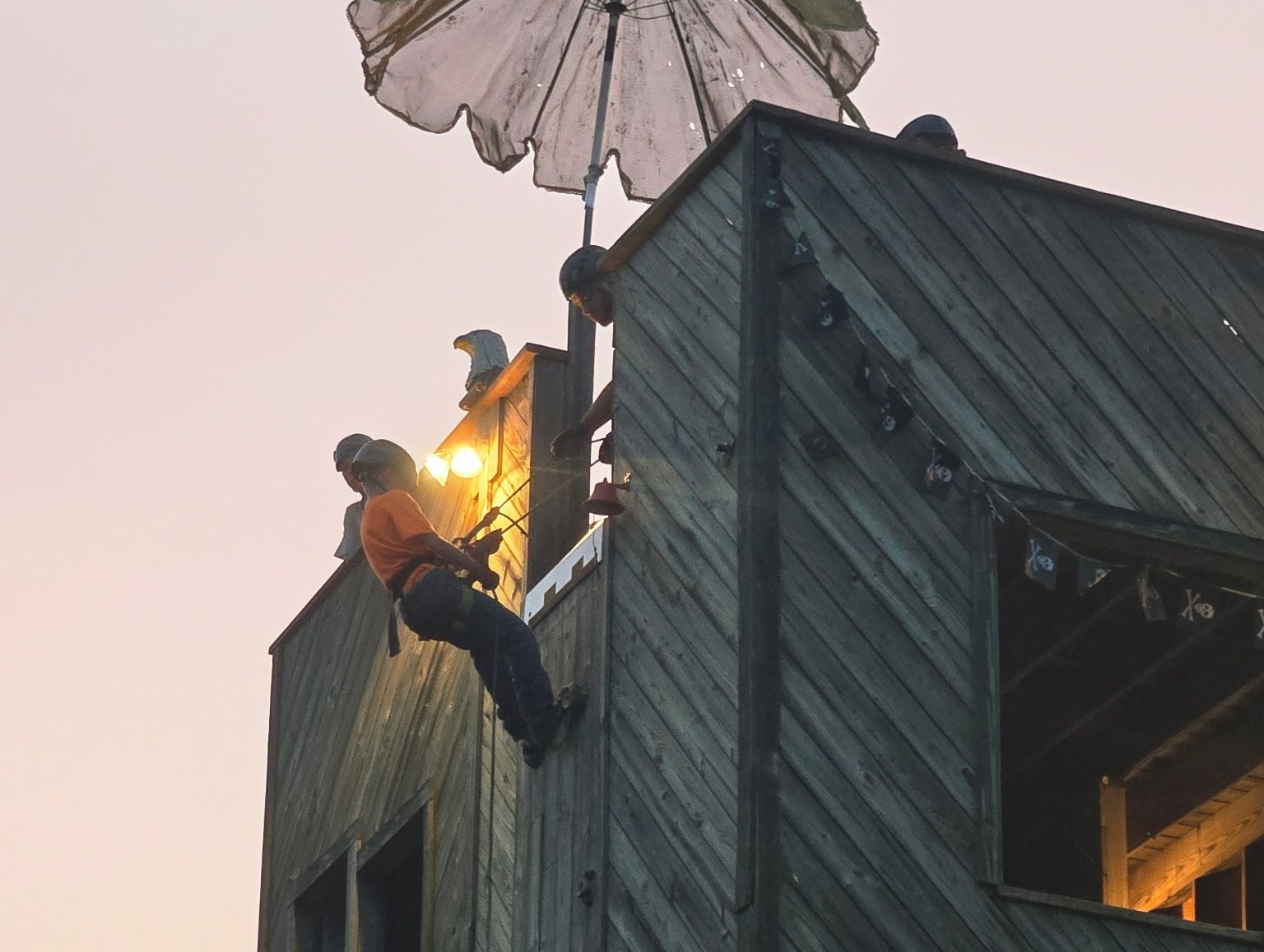 Person rappelling down a wooden structure with a parachute above.