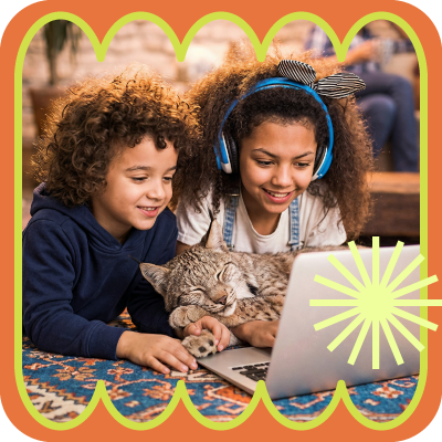 Children smiling while using a laptop with a cat in a cozy indoor setting