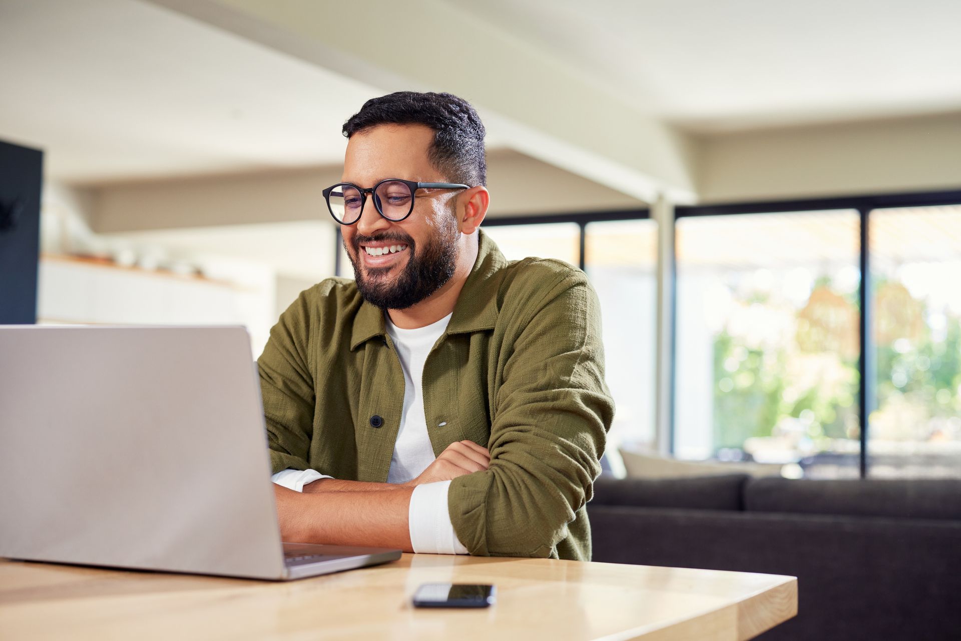 Smiling man working on a laptop at a table in a bright living room