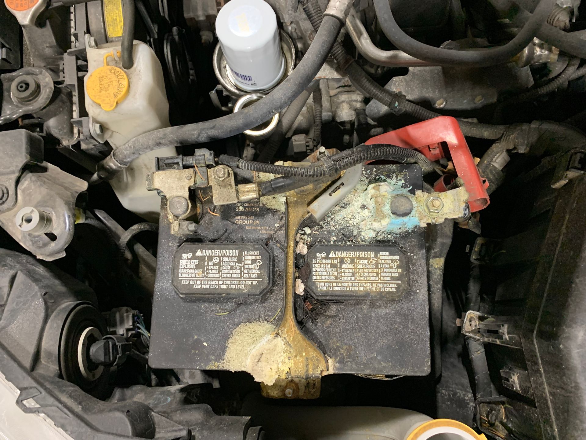 A dirty battery is sitting under the hood of a car. | Lou's Car Care Center Inc.