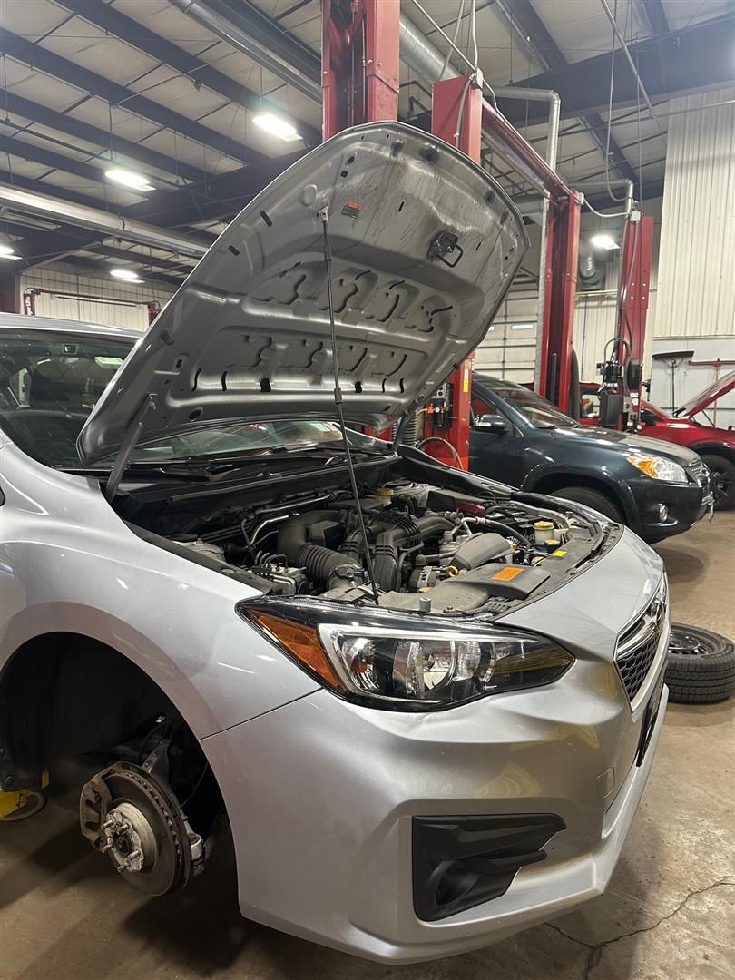 A silver car with the hood up in a garage. | Lou's Car Care Center