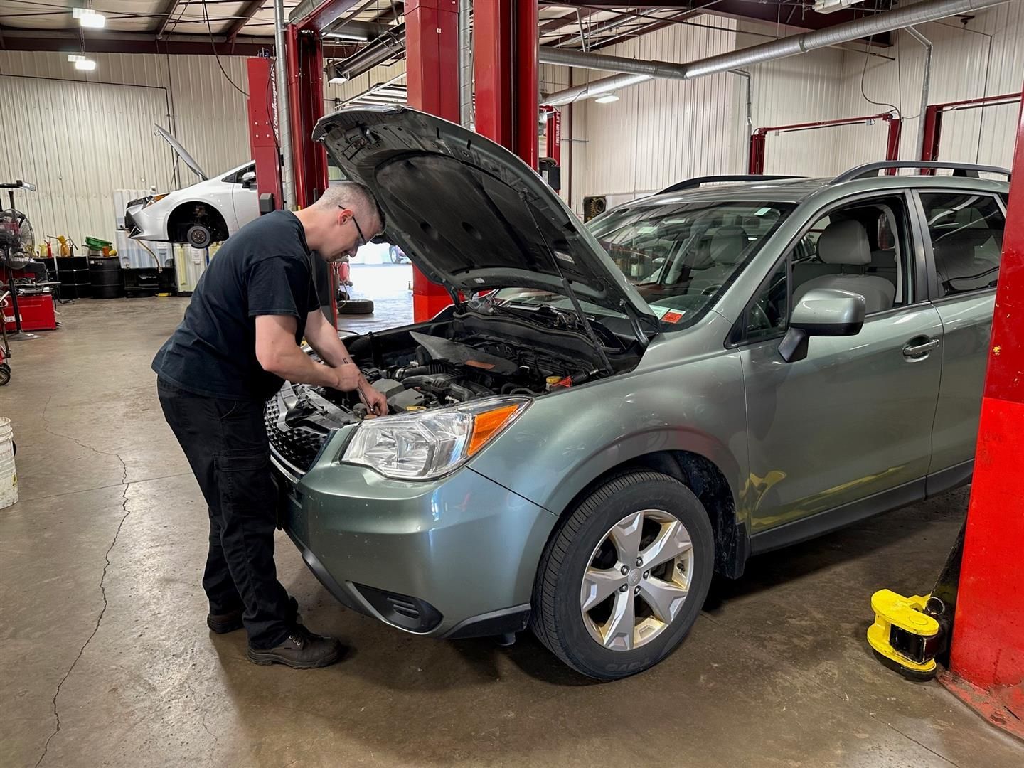 A man is working on the engine of a car in a garage. | Lou's Car Care Center Inc.