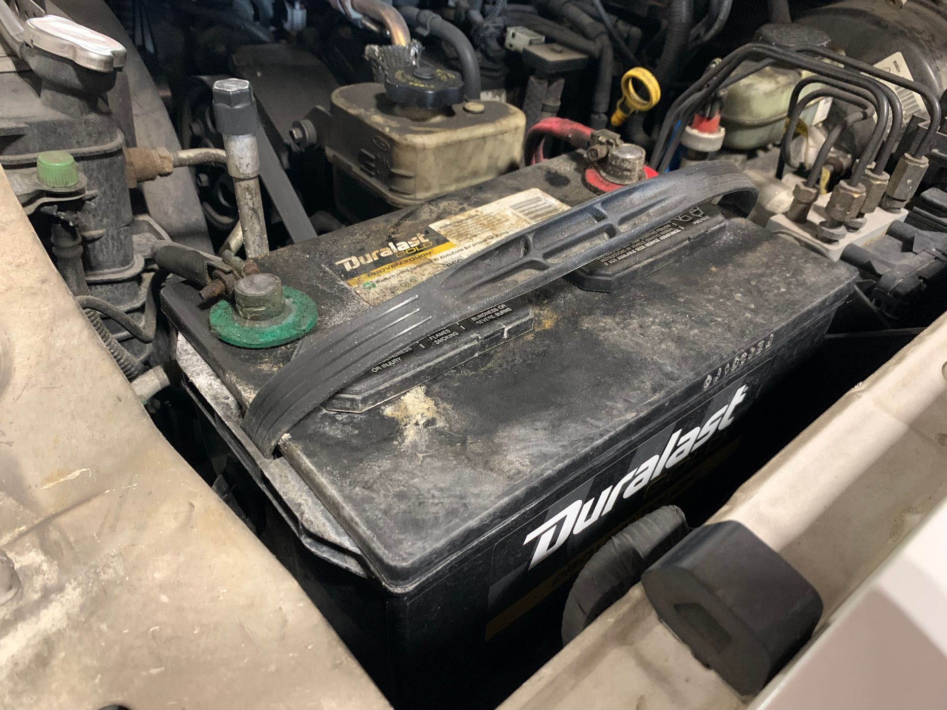 A car battery is sitting under the hood of a car. | Lou's Car Care Center Inc.
