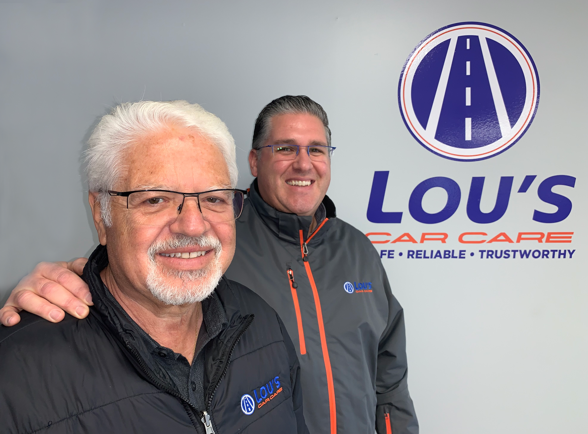 A group of men are standing around a car in a garage. | Lou's Car Care Center