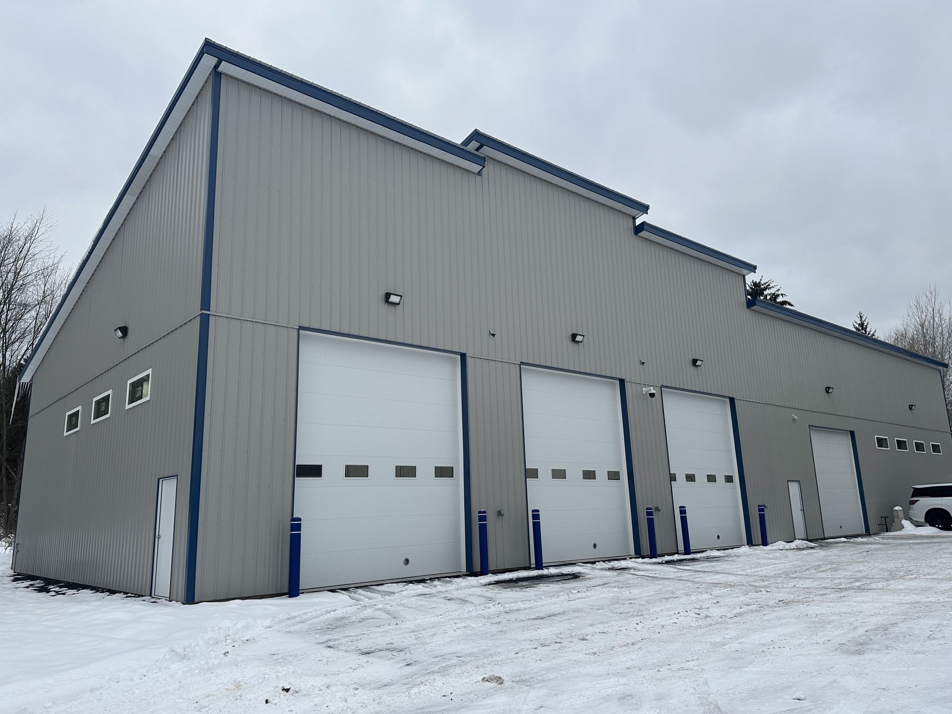 Gray building with three, white bay doors and a white man door with snow on the ground. | Lou's Car Care Center, Inc.
