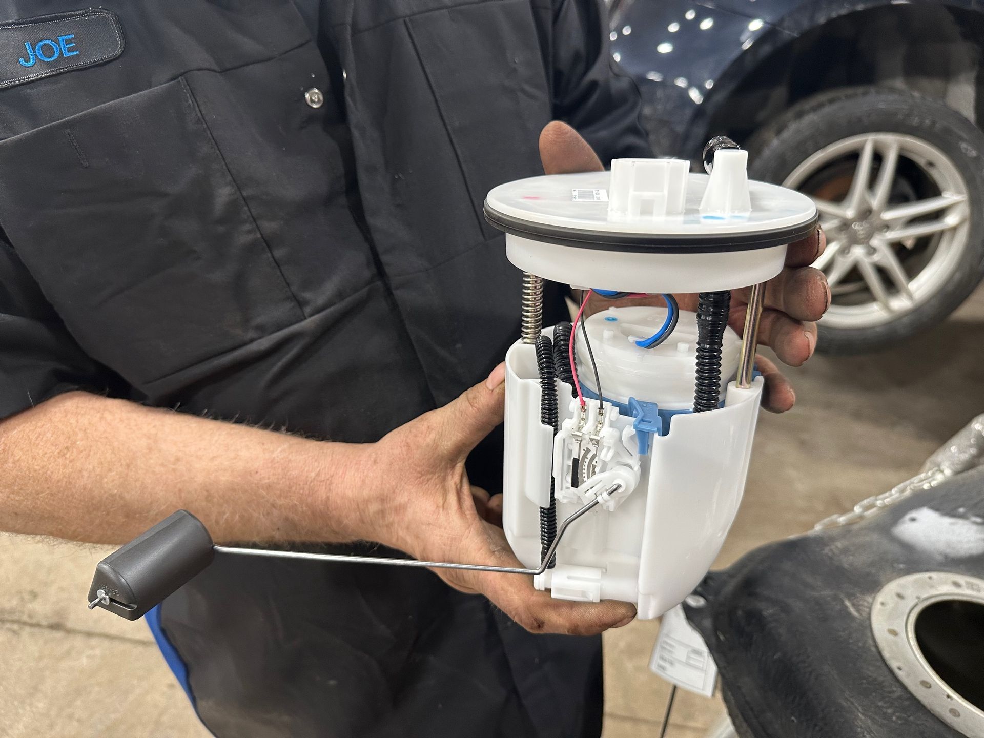 New fuel pump being held by auto technician wearing black and blue uniform | Lou's Car Care Center, Inc.