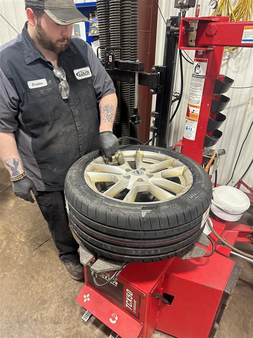 A man is changing a tire on a machine in a garage. | Lou's Car Care Center, Inc.